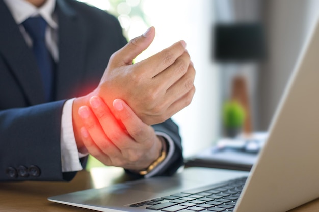 Businessman wearing suit hand holding wrist He felt his wrist hurt while woking with laptop on office desk at home He tends to feel pain in his wrist when sitting for a long time at work