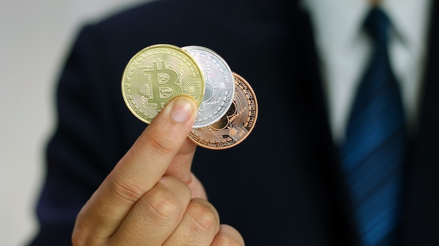 Businessman wearing a suit is showing bitcoins in his hand.