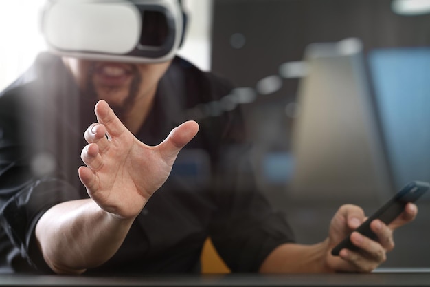 VRヘッドセットを使用して携帯電話で現代のオフィスでバーチャルリアリティゴーグルを身に着けているビジネスマン