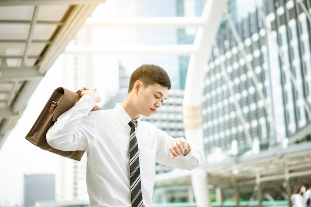 A businessman in white shirt is going to work in rush hour. He is looking at his watch. He want to go to office on time.