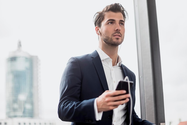 Businessman at the window with cell phone and earbuds