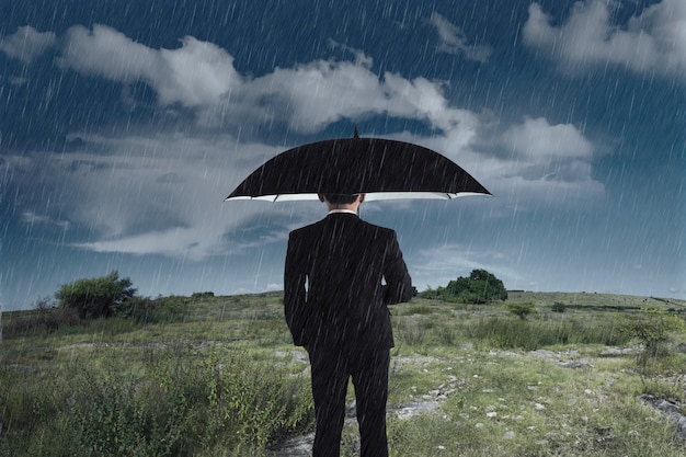 雨の中で立っている傘を持ったビジネスマン