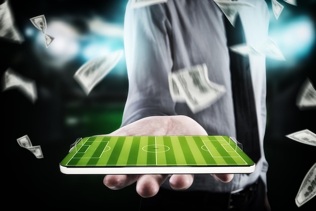 Businessman with banknotes around holds cellphone in his hand with a football field on the display