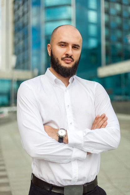 Businessman with beard in white shirt standing near office building