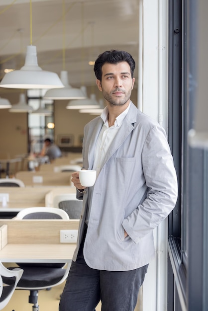 Foto uomo d'affari con una tazza di caffè che guarda fuori dalla finestra in ufficio