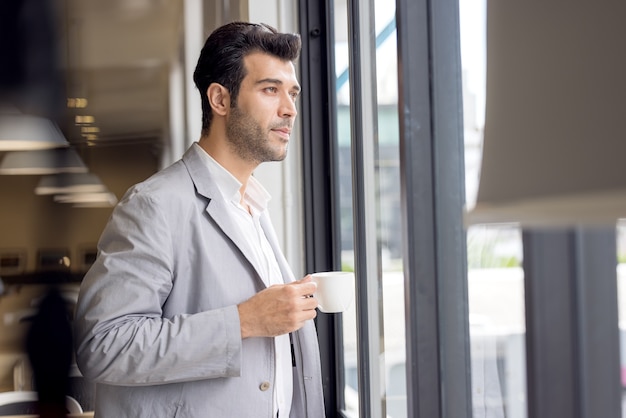 businessman with cup of coffee looking out of window at office