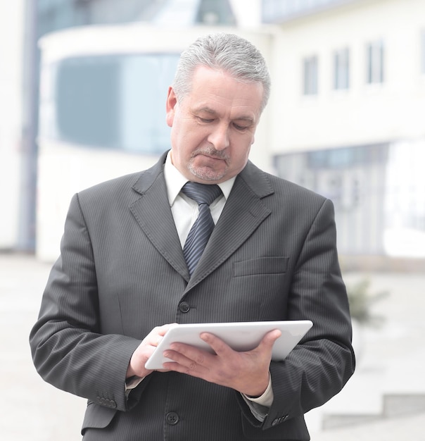 Businessman with digital tablet standing near office building