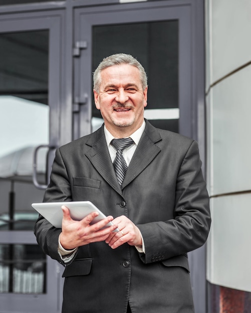 Businessman with digital tablet stands on the background of a modern office building