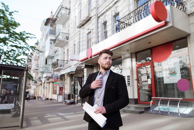 Бизнесмен с документами в руках стоит на улице у входа в офис
