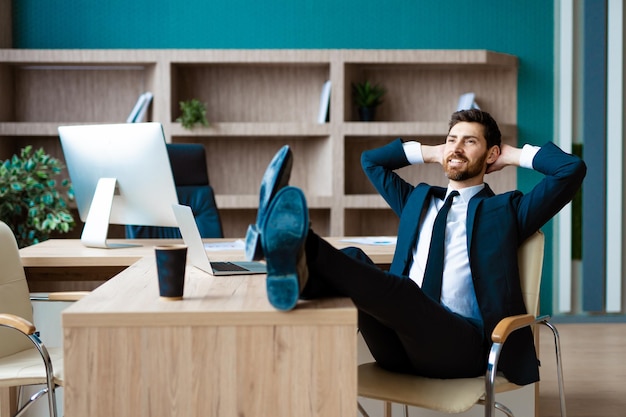 Businessman with elegant suit sitting at computer desk in the office - Adult man relax at work, concepts about business and technology