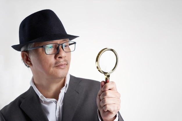 Businessman with hat holding magnifying glass against white background