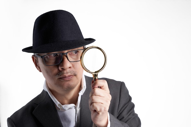 Businessman with hat holding magnifying glass against white background