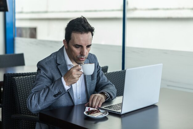 Uomo d'affari con il computer portatile che beve caffè nella caffetteria