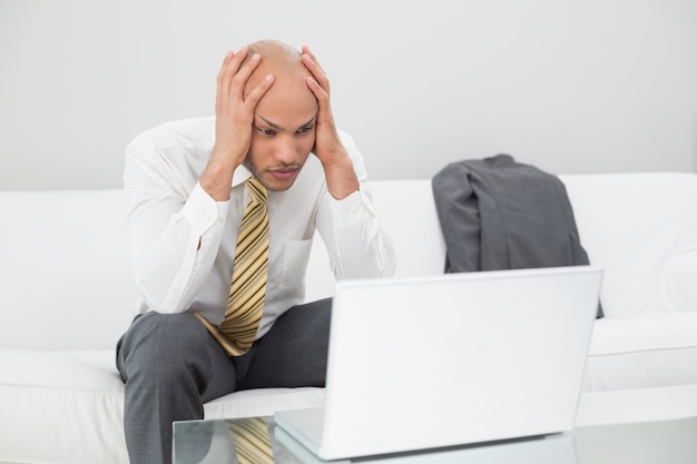 Businessman with laptop holding head in hands at home