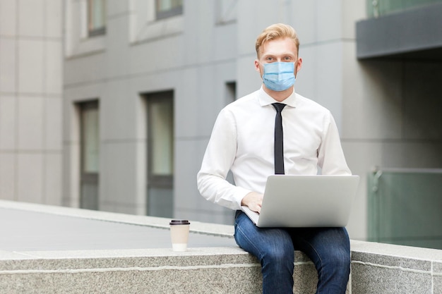 Businessman with medical mask in white shirt working on laptop outsourcing looking at camera