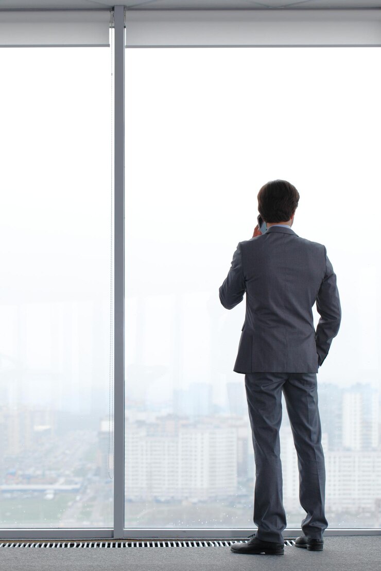 Businessman with mobile phone looking through window