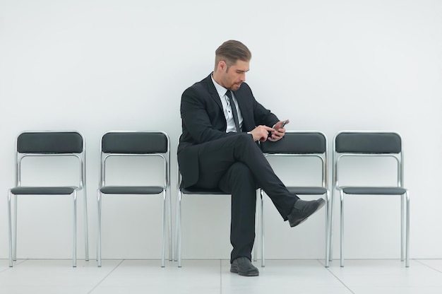 Бизнесмен с мобильным телефоном сидит в коридоре офиса