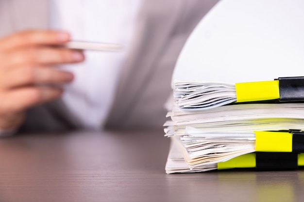 Photo a businessman with a pen in the background of a stack of documents held together by clamps