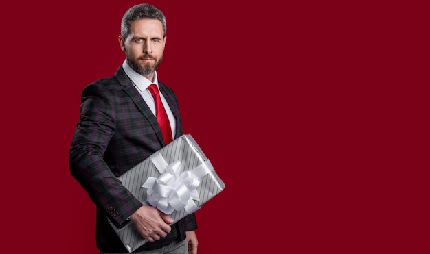 Бизнесмен с подарком изолирован на красном фоне