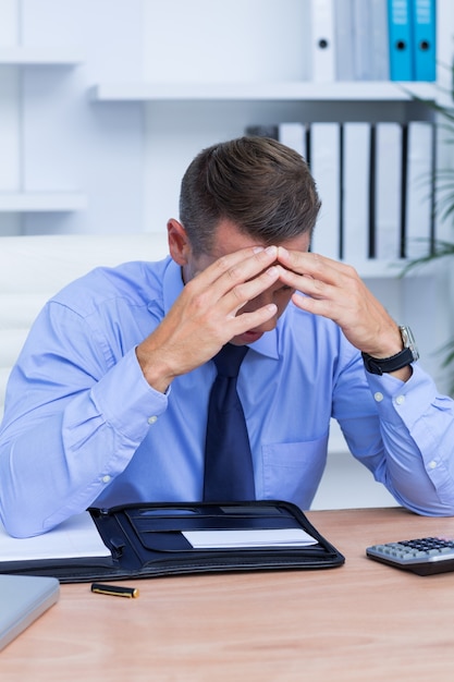 Businessman with severe headache sitting at office desk