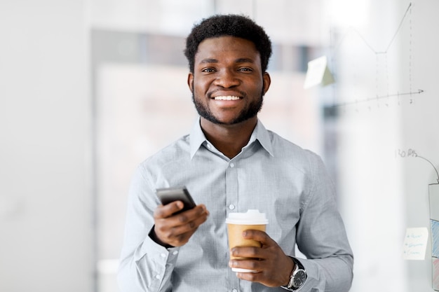 オフィスでスマートフォンとコーヒーを飲むビジネスマン