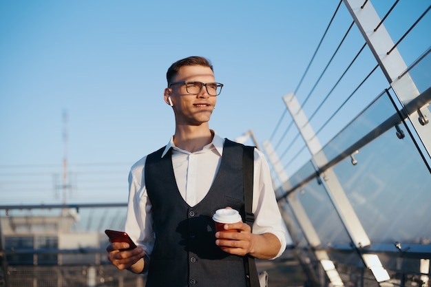 スマートフォンを持つビジネスマンは、オフィスのテラスでコーヒーを飲みます