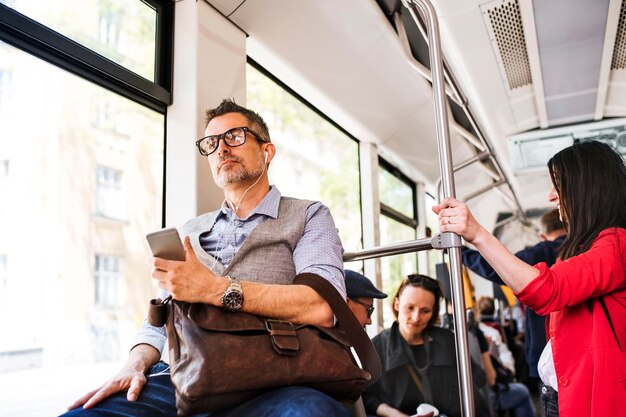 トラムで旅行しているスマートフォンとイヤホンを持つビジネスマン