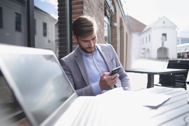 Businessman with a smartphone sitting at a table in a street cafepeople and technology