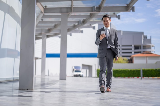 Uomo d'affari con lo smartphone che cammina contro la strada sfocata sullo sfondo dell'edificio, fashion business.