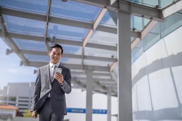 Uomo d'affari con lo smartphone che cammina contro la strada sfocata sullo sfondo dell'edificio, fashion business.