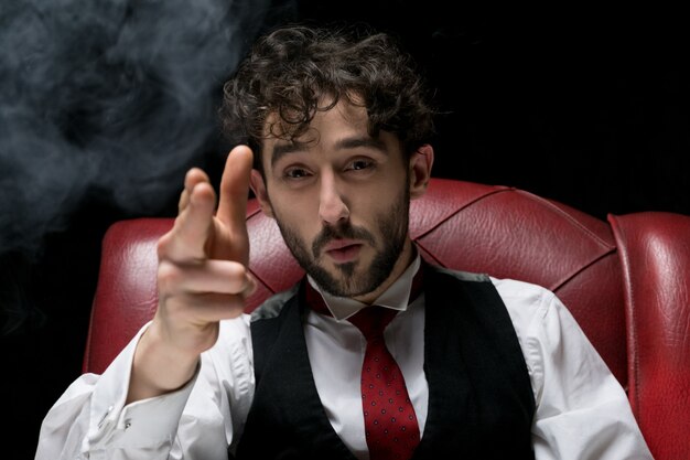 Photo businessman with smoking gun finger red. red chair on a black background