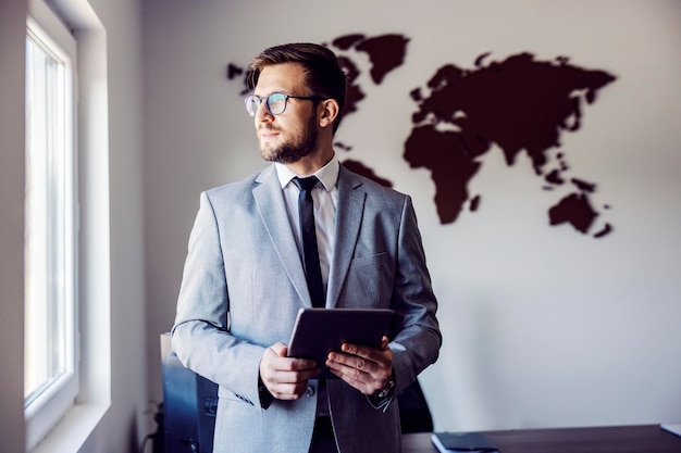 A businessman with tablet posing in the office near the window