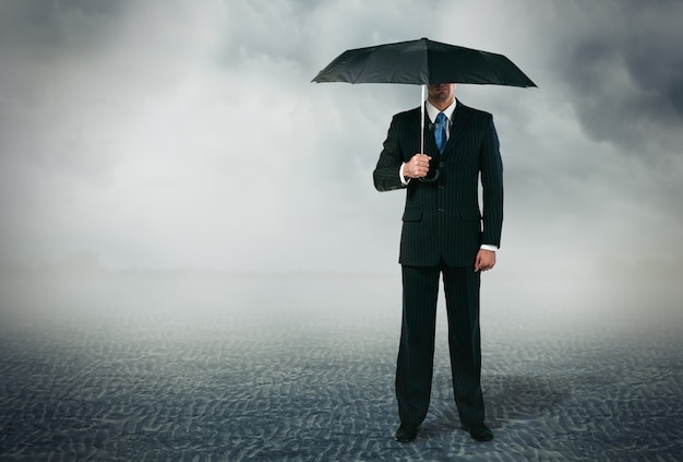 Businessman with umbrella standing at cloudy background