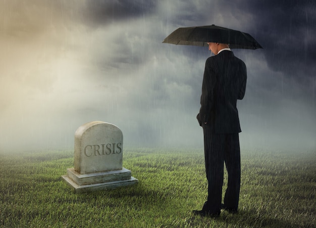 Businessman with umbrella standing near tomb of crisis