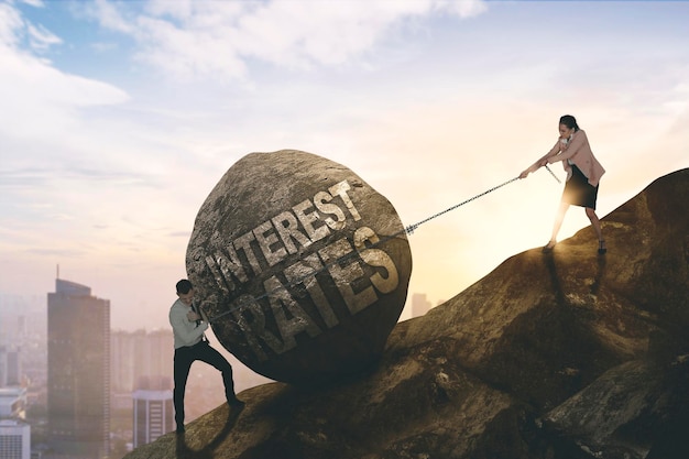 Businessman and woman pulling a stone with interest rates text to climb up a hill