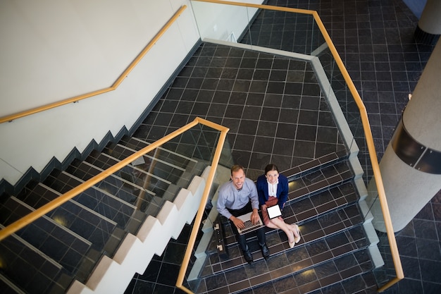 Businessman and woman sitting on steps using laptop and digital tablet