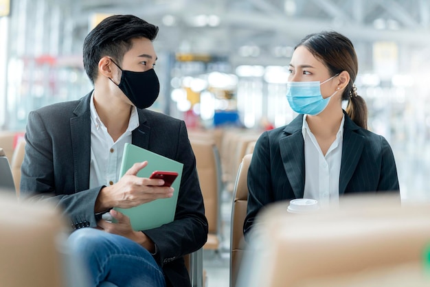 공항 터미널의 새로운 라이프스타일 비즈니스 개념에 있는 사회적 거리 좌석에서 얼굴 마스크 보호 캐주얼 회의를 가진 사업가와 여성