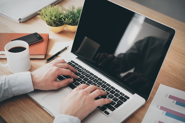 Businessman at work. Close-up top view of man working on laptop while sitting at the wooden desk