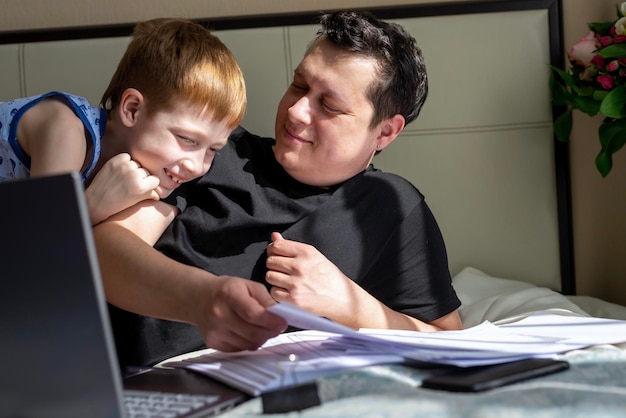 Businessman working on a laptop computer sitting at home and working with documents dad working at home Child son next to father Freelancing home office