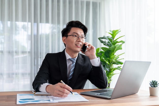 Businessman working on laptop at office desk and talking on the phone Jubilant