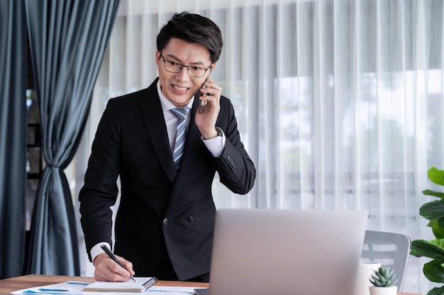 Businessman working on laptop at office desk and talking on the phone Jubilant