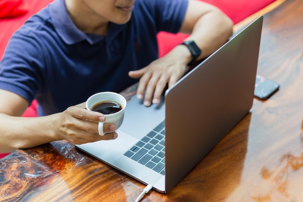 Uomo d'affari che lavora al computer portatile con la tazza di caffè della tenuta della mano