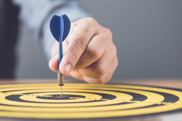 Businessman working in the office and throwing arrow darts in the center of yellow dartboard Goal and success for business concept