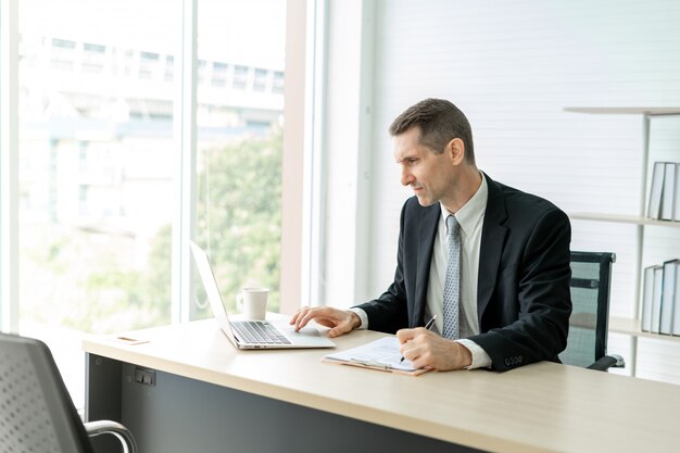 Photo businessman working seriously on laptop at desk in office