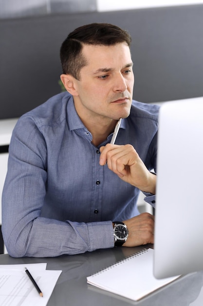 Businessman working with computer in modern office. Headshot of male entrepreneur or company director at workplace. Business concept.