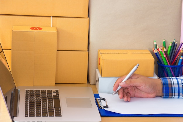 Businessman working with mobile phone and packing brown parcels box at home office