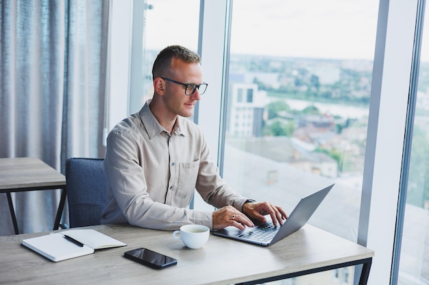 A businessman works on a laptop a manager sits at a table in the office works on a laptop Freelancer workplace employee at remote work Remote workplace in coworking cafe