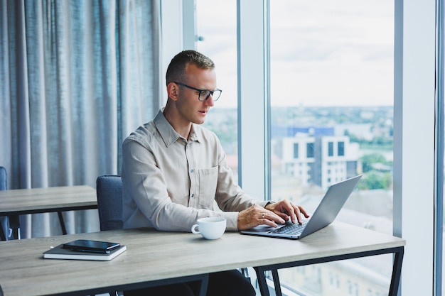 A businessman works on a laptop a manager sits at a table in the office works on a laptop Freelancer workplace employee at remote work Remote workplace in coworking cafe