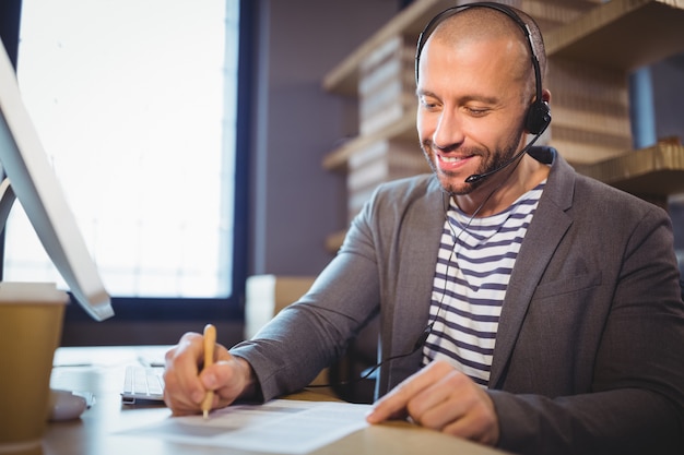 Businessman writing on paper while talking with headphones