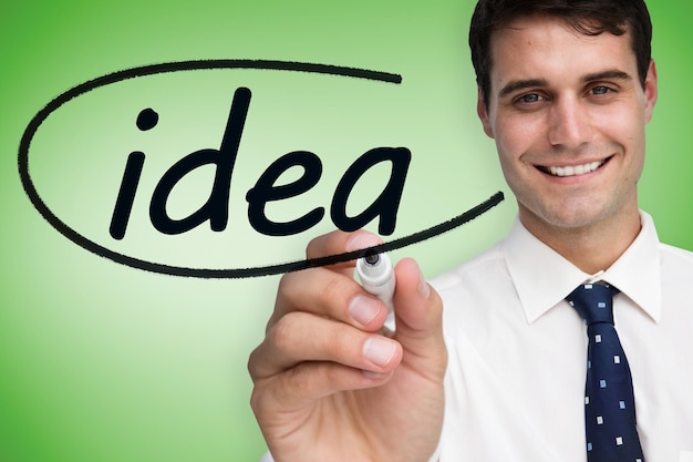 Businessman writing the word idea against green vignette